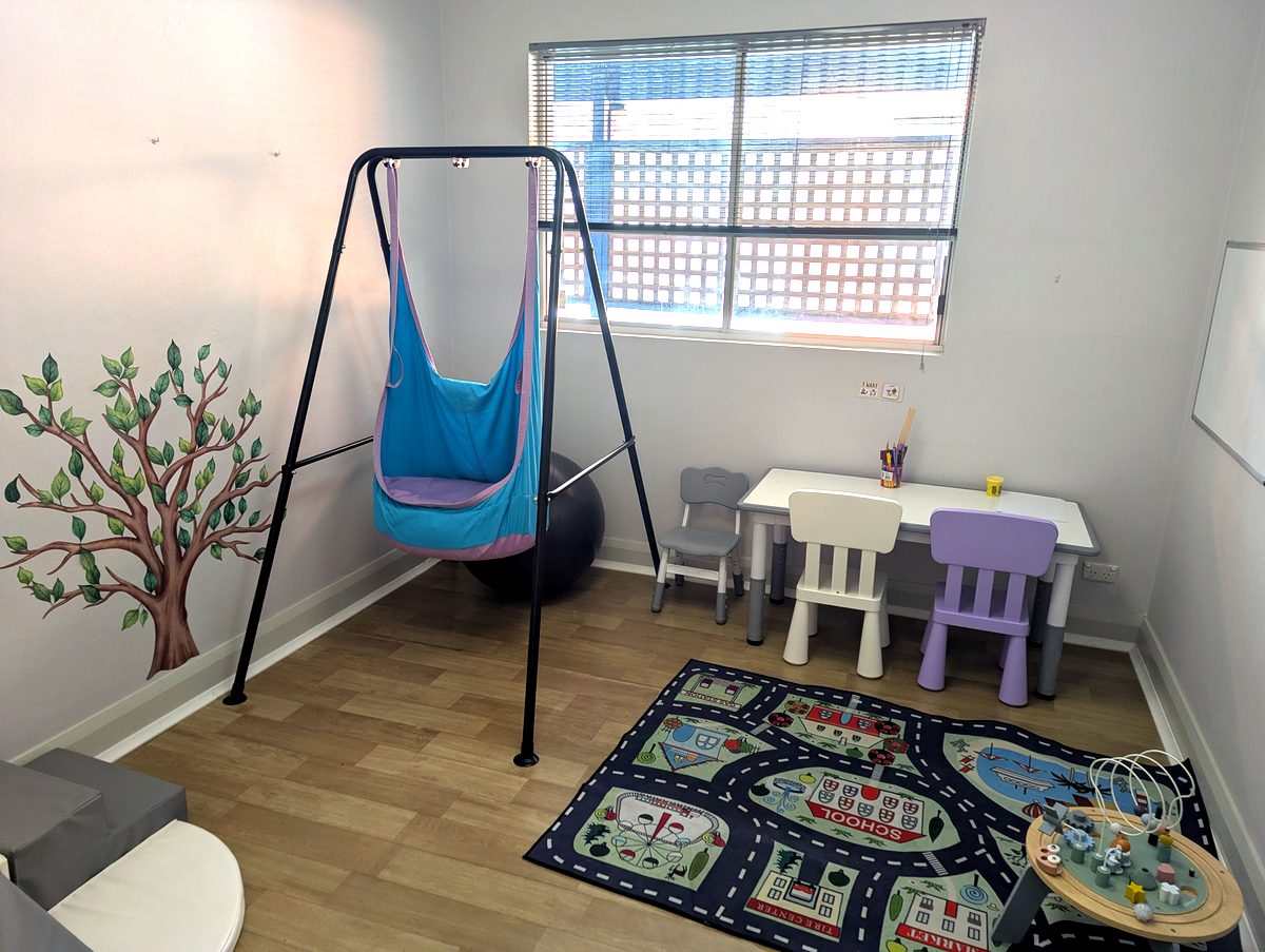 Therapy room with a sensory swing, exercise ball, kids' table and play mat for movement and language sessions